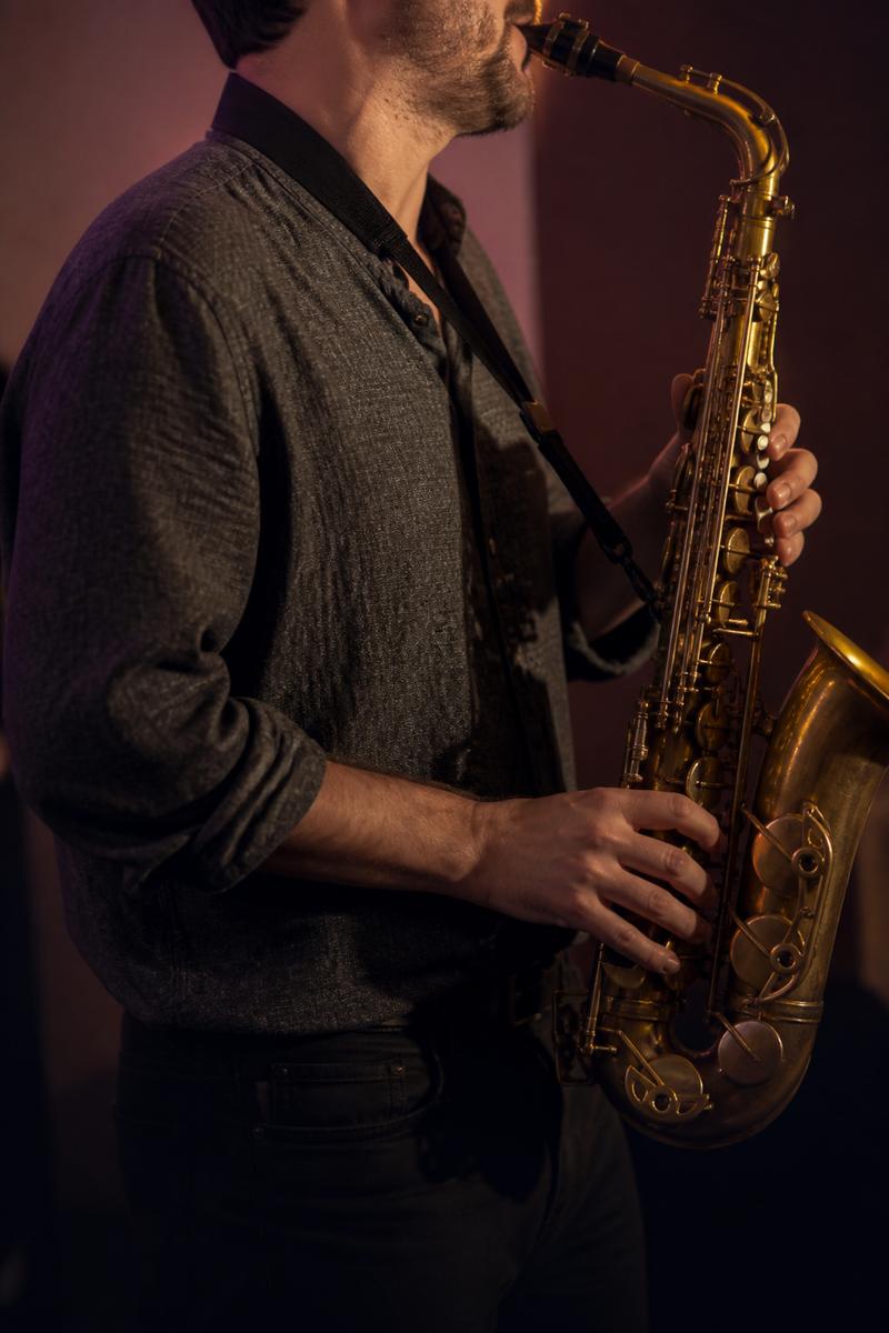 Adult playing alto saxophone in soft light